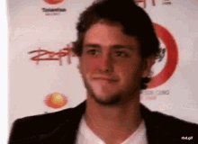 a man with a beard is smiling in front of a sign that says " rbd.gif "
