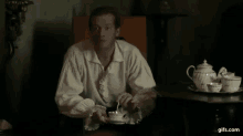 a man sits at a table with a tea set and says " parce que j'avais oublie votre nom "