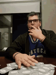 a man smoking a cigar while wearing a blue shirt that says ' atuca ' on it