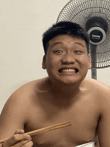 a shirtless man holds chopsticks in front of a benny brand fan