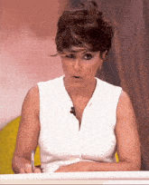 a woman in a white sleeveless shirt is sitting at a table with a pen in her hand