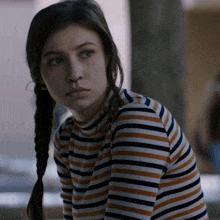 a girl with pigtails wearing a striped shirt looks at the camera with a serious look on her face