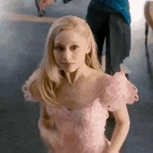 a young girl in a pink dress is standing in a room with a man standing behind her .