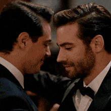 two men in suits are touching their foreheads and smiling