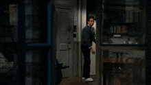 a man in a grey sweater is standing in a doorway looking out a window