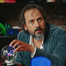 a man with a beard is playing with a sphere with a purple light inside of it
