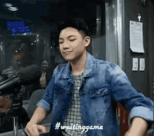 a young man in a denim jacket is standing in front of a microphone in a radio studio .