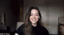 a woman in a black shirt is smiling and the name aubrey plaza is on the bottom right