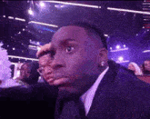 a man in a suit and tie is making a funny face while sitting in a theatre .