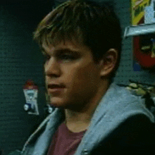 a young man wearing a hoodie and a red shirt is standing in front of a wall with holes in it .