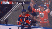 a hockey player holds a hockey stick in front of a banner that says goal
