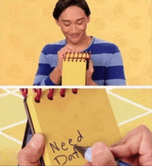 a man is holding a yellow notebook that says need dat on it