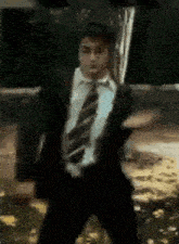 a man in a suit and tie is dancing in front of a green board .