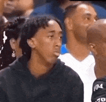 a man is making a funny face while sitting in the stands during a basketball game .