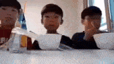 three young boys are sitting at a table with bowls of food and spoons .