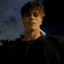 a young man wearing a black shirt and a necklace looks at the camera at night .