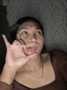 a woman in a brown shirt is making a funny face with her hand
