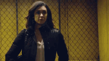 a woman in a black jacket is standing in front of a chain link fence