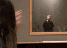 a woman looks at herself in a mirror with a man behind her
