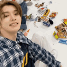 a young man in a plaid shirt is sitting on the floor surrounded by candy