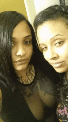 two women are posing for a picture together and one of them has a tattoo on her arm .