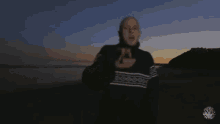 a man in a black sweater is standing on a beach at sunset
