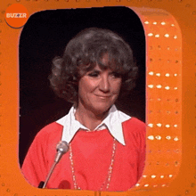 a woman in a red shirt stands in front of a microphone with buzzr written on the corner