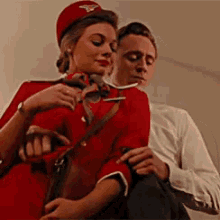a man and a woman are sitting next to each other . the woman is wearing a red uniform .
