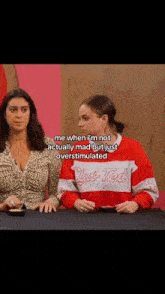 two women are sitting at a table and one of them is wearing a red and white sweater that says club ted .