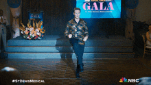 a man is standing on a stage in front of a screen that says gala