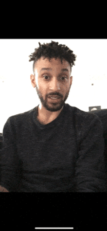 a man with a beard is wearing a grey sweater and making a surprised face