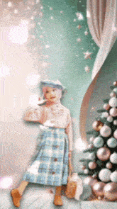 a girl in a plaid skirt stands in front of a decorated christmas tree