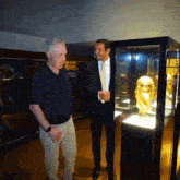 two men are looking at a trophy in a glass case with a sign behind them that says stadium