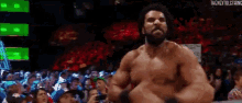 a shirtless man with a beard is standing in front of a crowd of people .