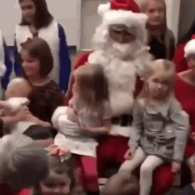 a group of people are sitting in a room with santa claus and a little girl .