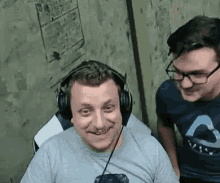 a man wearing headphones and glasses is smiling while another man stands behind him .