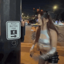 a woman in a silver top is walking past a push button for pedestrians