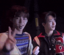 two young men are standing next to each other in a dark room . one of the men is wearing a microphone in his mouth .