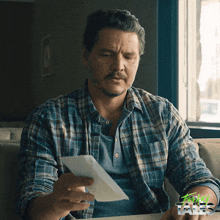 a man in a plaid shirt is looking at a piece of paper with the word tales on the bottom
