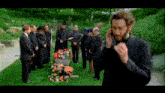a man in a black suit is talking on a cell phone in front of a funeral
