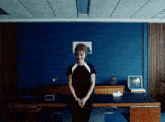 a woman stands in front of a desk in a blue room