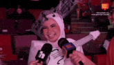 a woman in a costume with a guitar on her head is being interviewed by a person holding a rode microphone