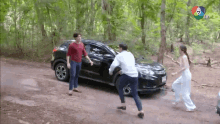 a man and a woman are fighting in front of a black car on a dirt road .