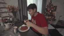 a young man is sitting at a table eating pancakes .