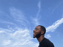 a man in a black shirt is smiling in front of a blue sky with white clouds