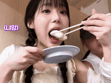 a girl with pigtails is eating food with chopsticks with a purple sticker that says ' l' ' on it