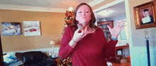 a woman is holding a donut in her hand in front of a christmas tree in a living room .