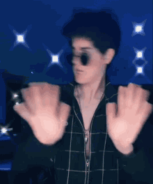 a man wearing sunglasses and a plaid shirt is making a gesture with his hands .