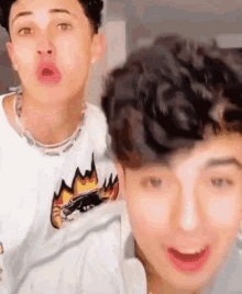 two young men are standing next to each other and making funny faces . one of the men is wearing a necklace .