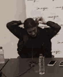 a man with a beard is sitting at a table with his hands behind his head .
